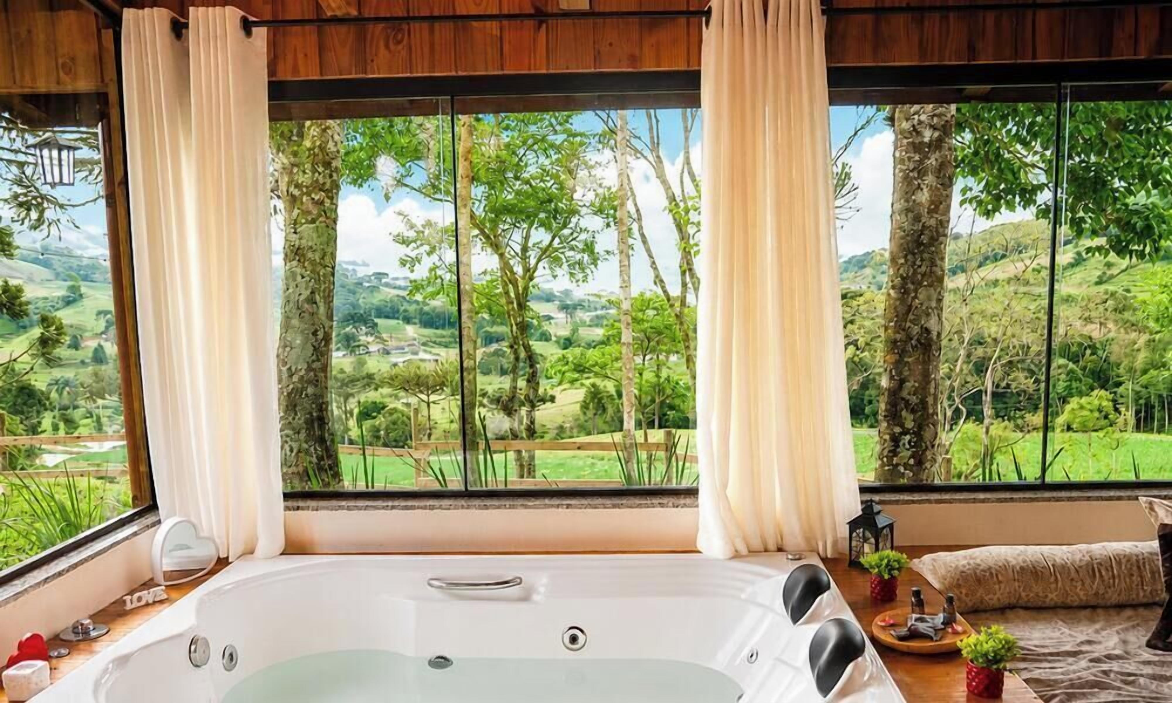 Quarto com uma grande janela, banheira e vista para uma paisagem verde.