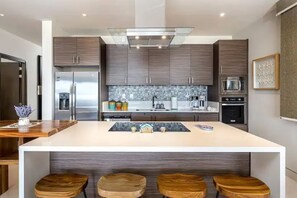 Uma cozinha moderna com ilha central, banquetas de madeira e eletrodomésticos de aço inoxidável.
