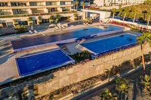 Piscina no terraço com várias áreas, rodeada por palmeiras e um jardim ajardinado.