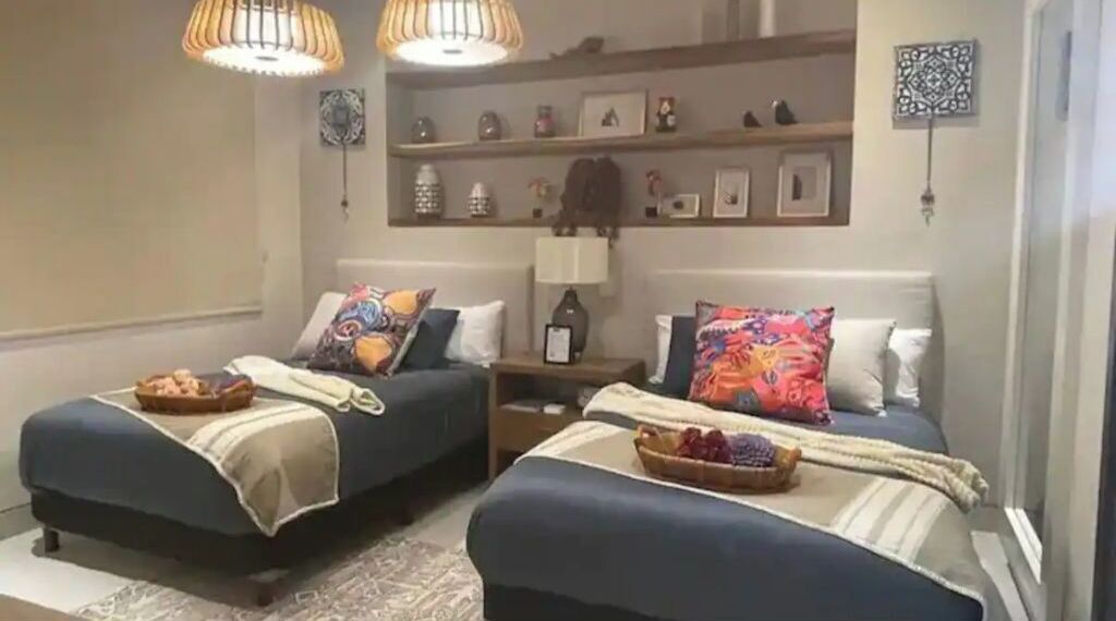 Une chambre avec deux lits, une table de chevet, une lampe et des étagères ornées d’objets décoratifs.