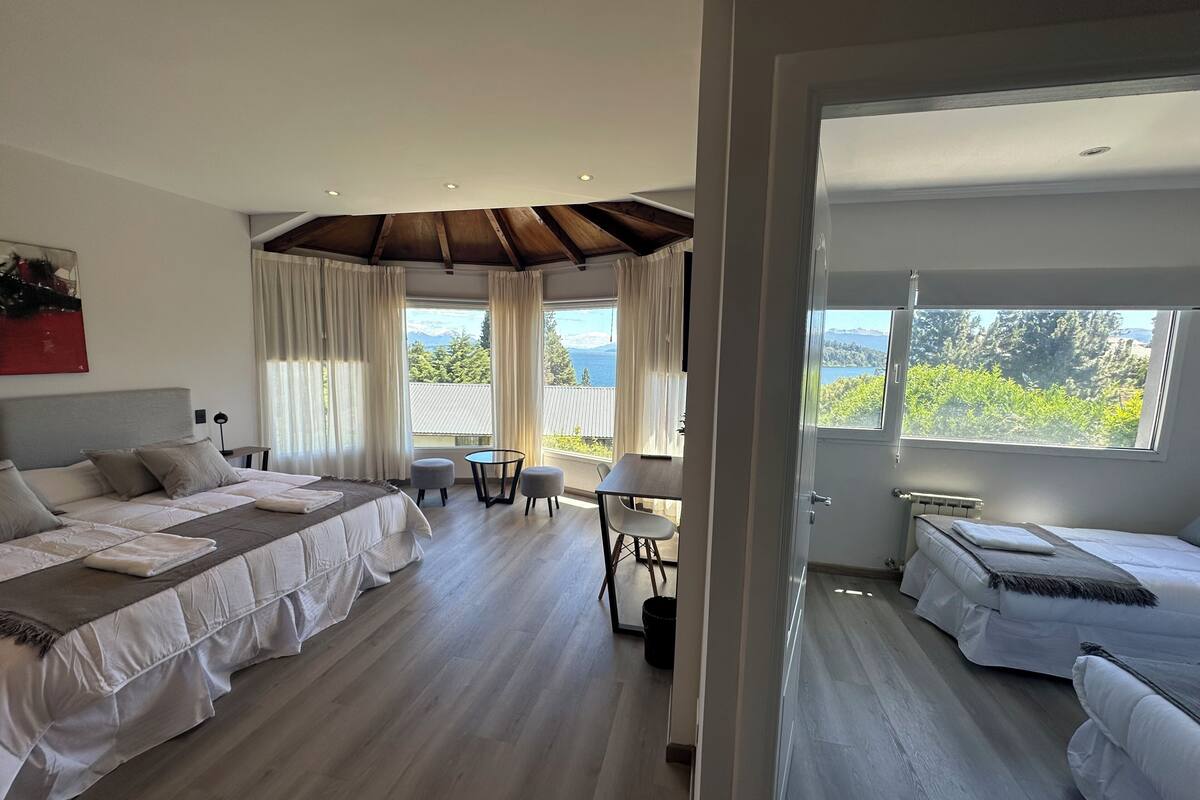 Ein modernes Hotelzimmer mit einem großen Bett, einem kleineren Bett, einem Essbereich und Blick ins Freie.