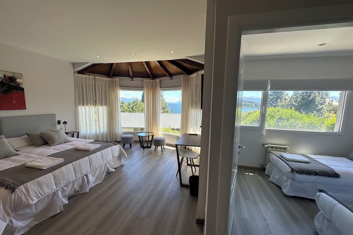 Una habitación de hotel moderna con una cama grande, una cama más pequeña, un área de comedor y vistas al exterior.