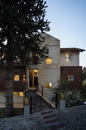 A modern two-story house with a stone facade, wooden accents, and a staircase leading to the entrance.