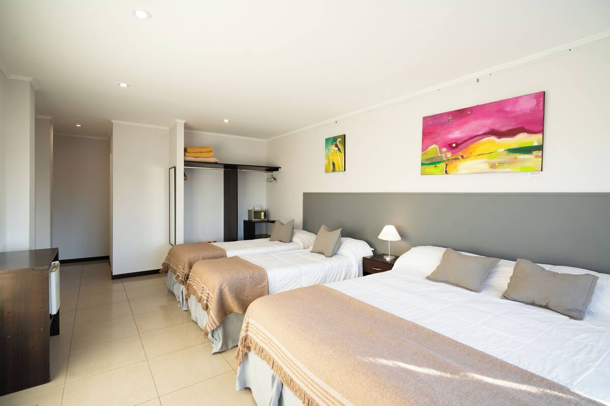 Una habitación de hotel con tres camas, un escritorio y un armario.