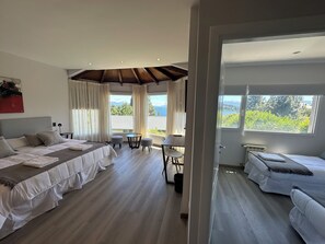 Ein modernes Hotelzimmer mit einem großen Bett, einem kleineren Bett, einem Essbereich und Blick ins Freie.