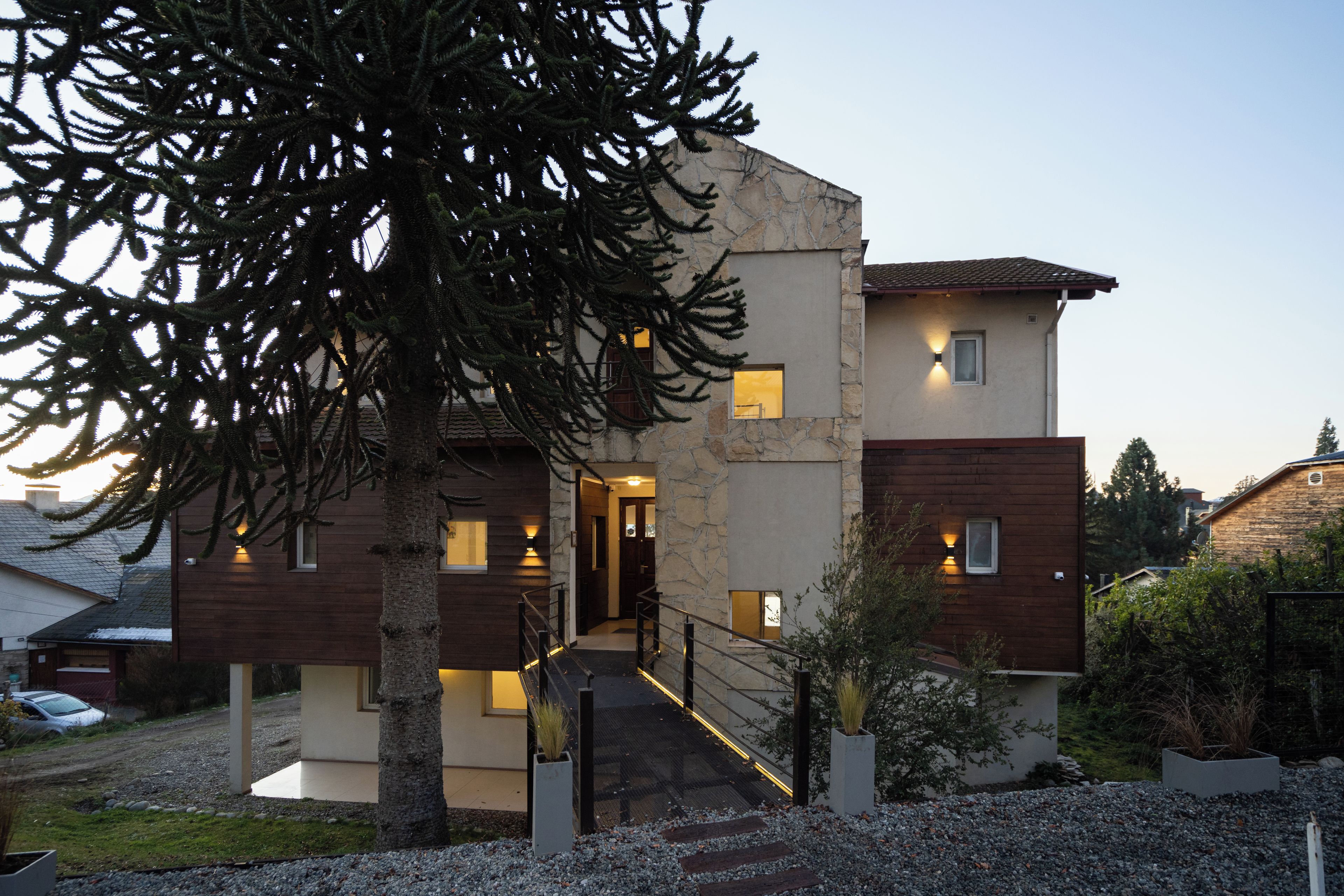 A modern two-story house with a stone facade, wooden accents, and a gravel driveway.