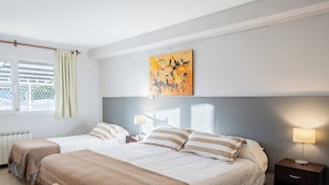 Et hotelværelse med to senge, et vindue med gardiner, en radiator, et billede på væggen og et natbord med en lampe.