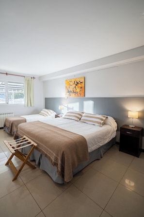 A bedroom with two beds, a window with curtains, a radiator, a painting on the wall, and a bedside table with a lamp. - NBH Lacus Boutique Hotel (San Carlos de Bariloche)