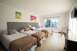 Hotellihuone, jossa on kolme sänkyä, työpöytä, televisio ja suuret ikkunat, joista on näkymä.