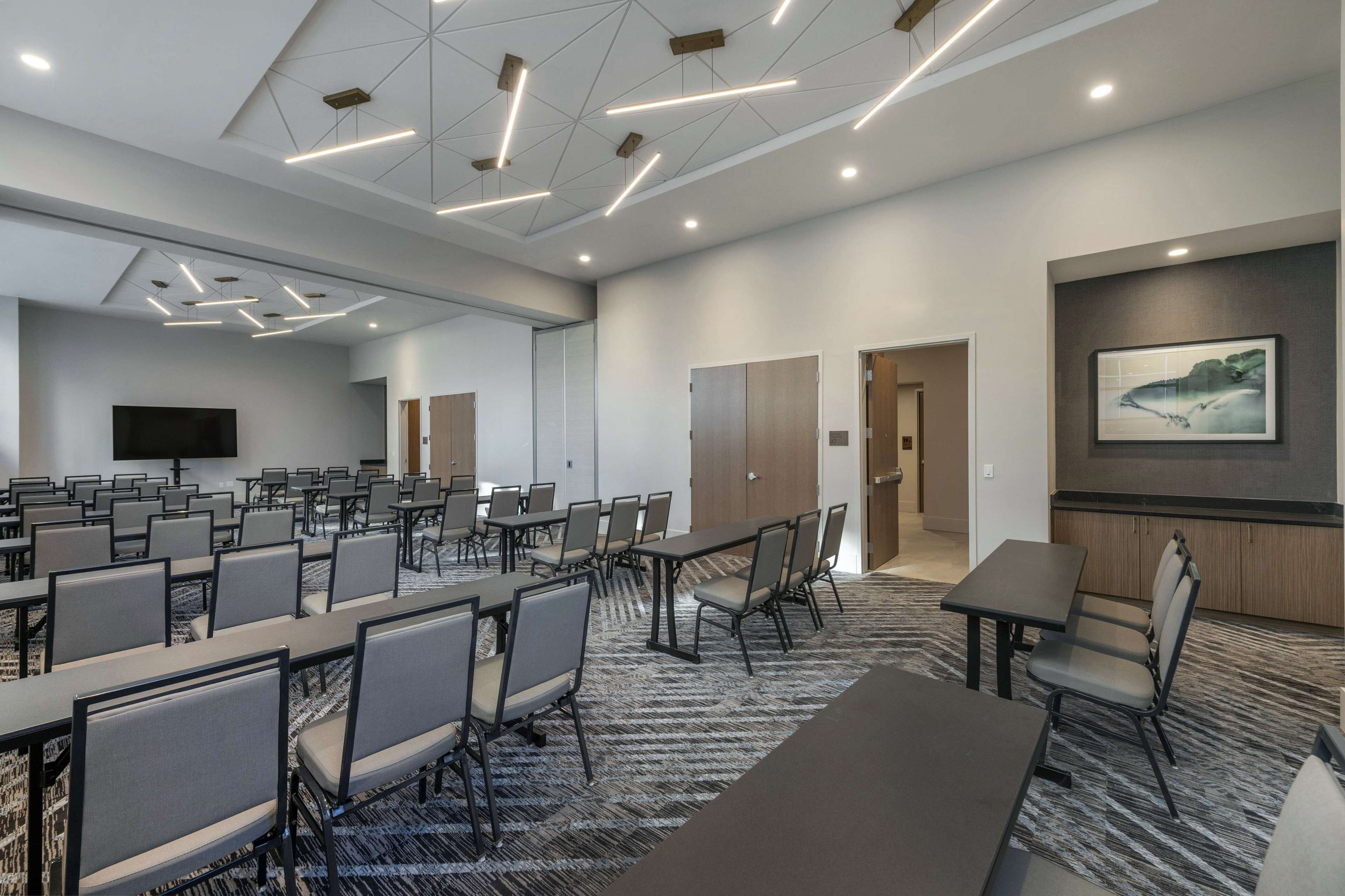 A conference room with multiple tables and chairs, a large screen, and a patterned carpet.