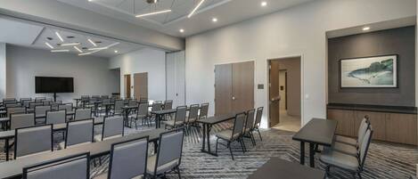 A conference room with multiple tables and chairs, a large screen, and a patterned carpet.