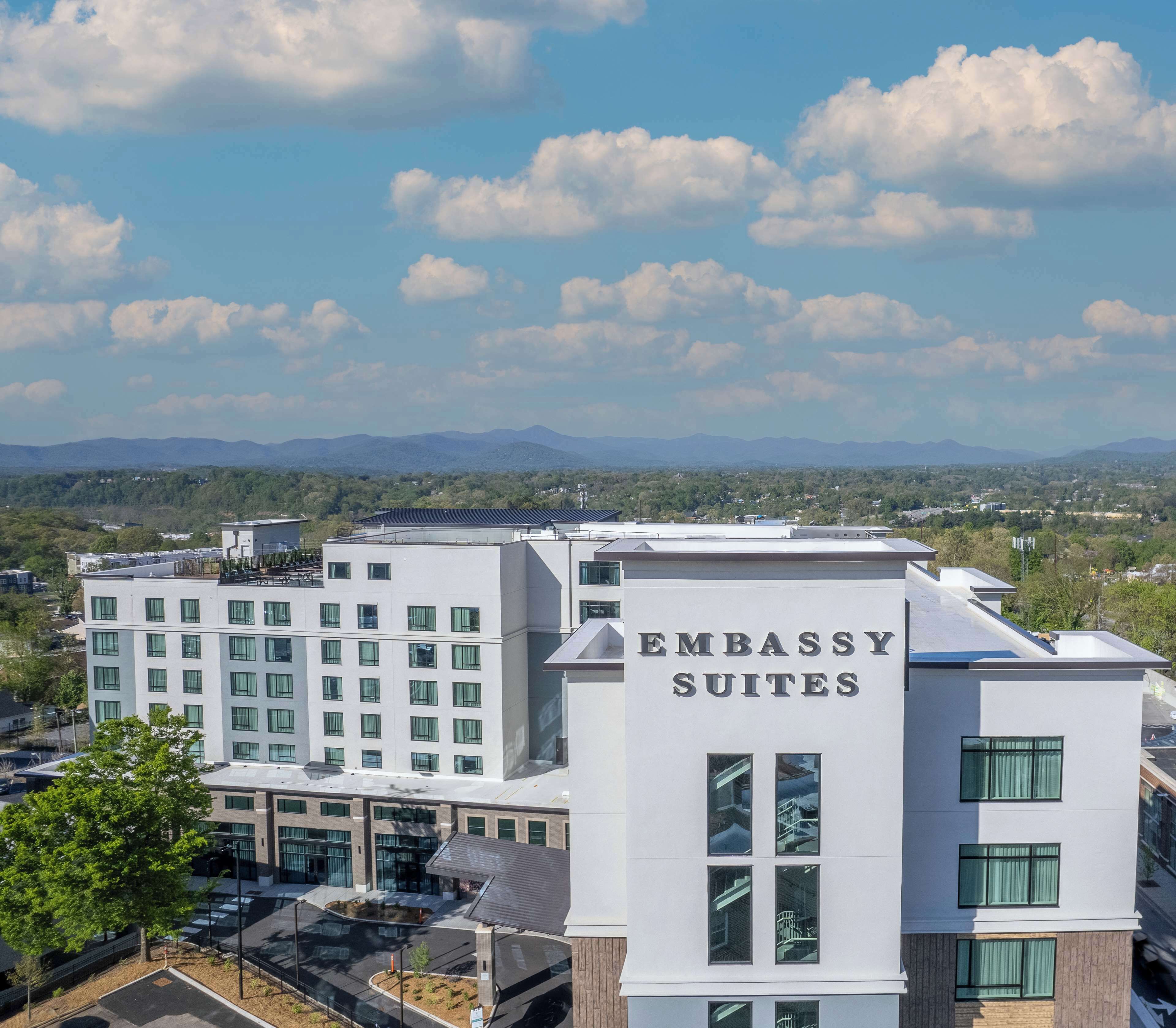 Een modern gebouw met een bord waarop 'Embassy Suites' staat. Het heeft een plat dak, meerdere ramen en een parkeerplaats ervoor.
