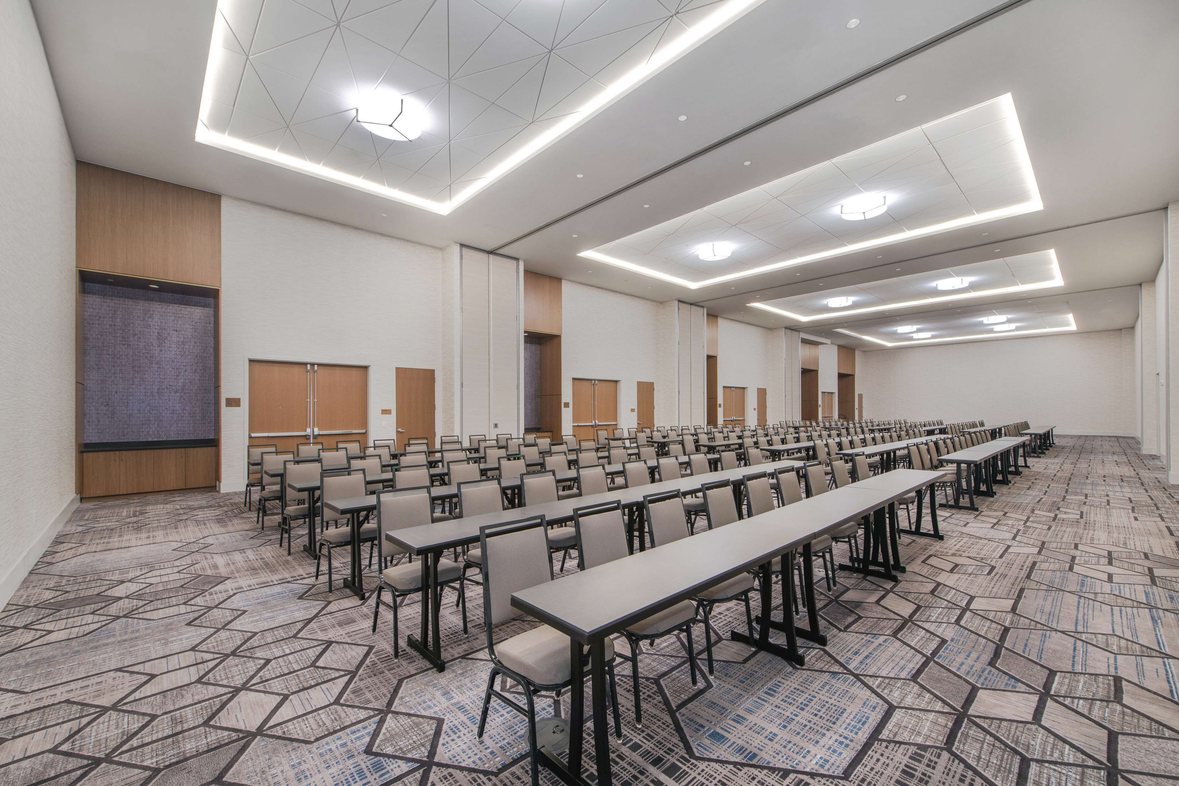 A conference room with rows of tables and chairs, a patterned carpet, and recessed ceiling lighting.