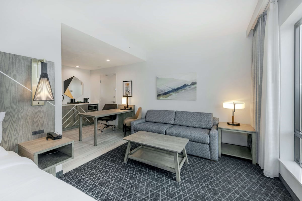 A modern hotel room with a sofa, a desk, a lamp, and a bed.