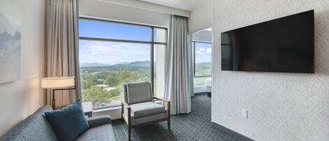 Una habitación de hotel con un ventanal grande, un televisor de pantalla plana, un sofá y una silla.