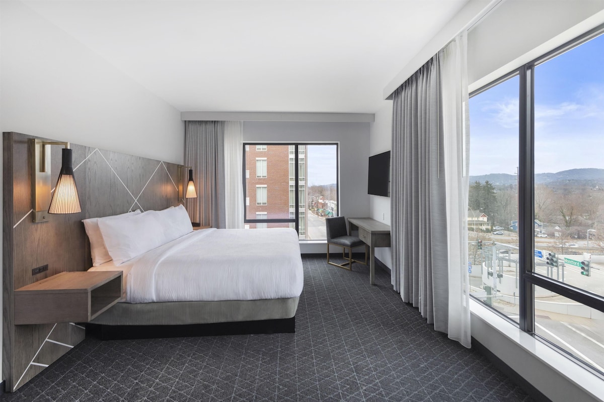 A modern hotel room with a large bed, a desk, and a TV.