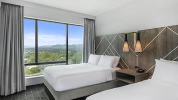 A hotel room with two beds, a large window with a view of mountains, and modern wall-mounted lighting.