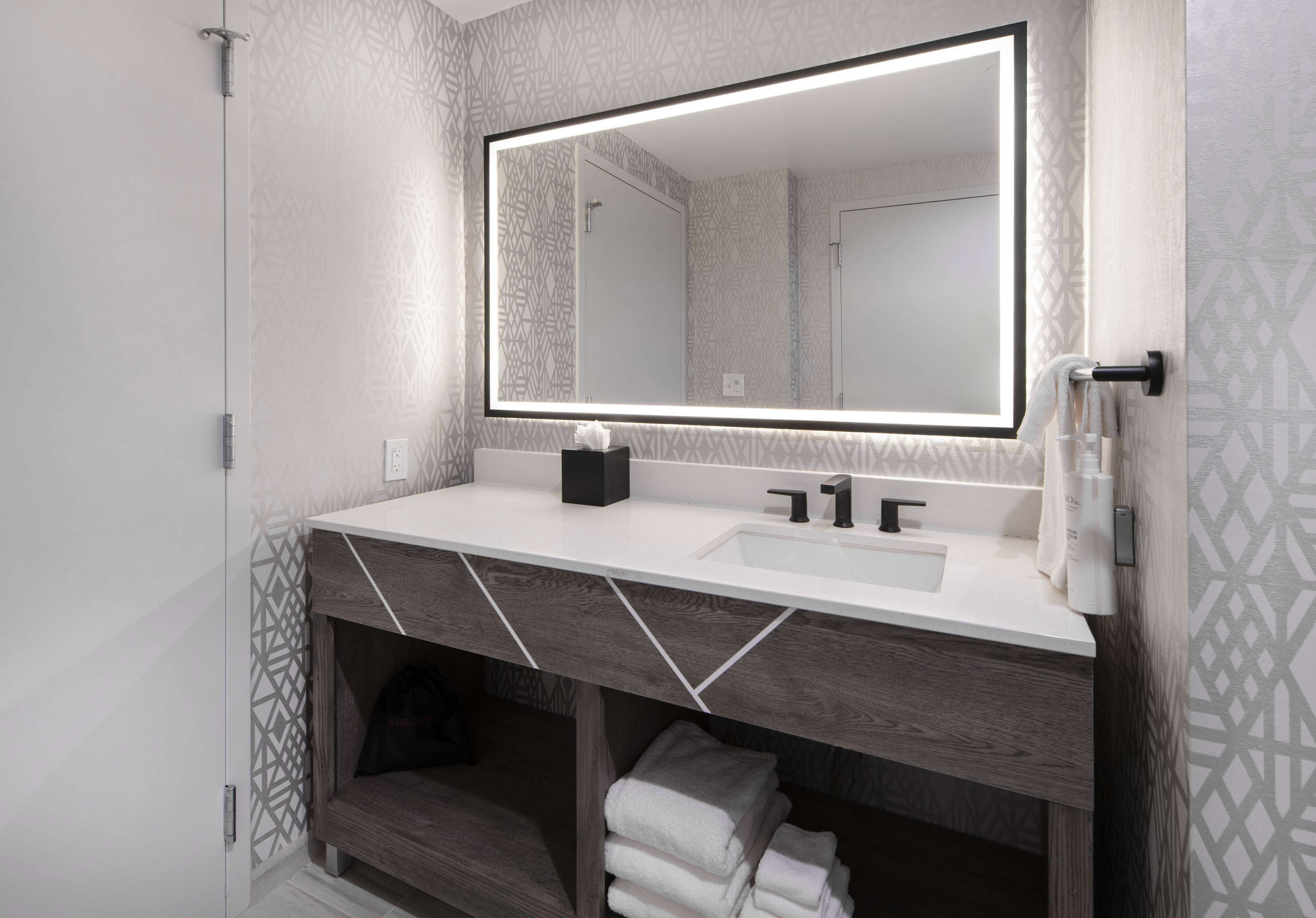 Une salle de bain moderne avec un grand miroir, un lavabo blanc et un meuble-lavabo en bois.