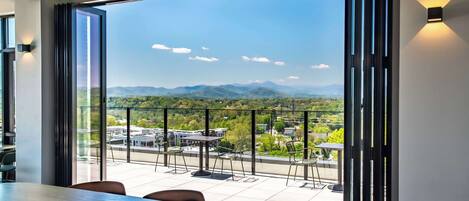 A modern dining area with a large table, chairs, and a view of mountains through large windows.