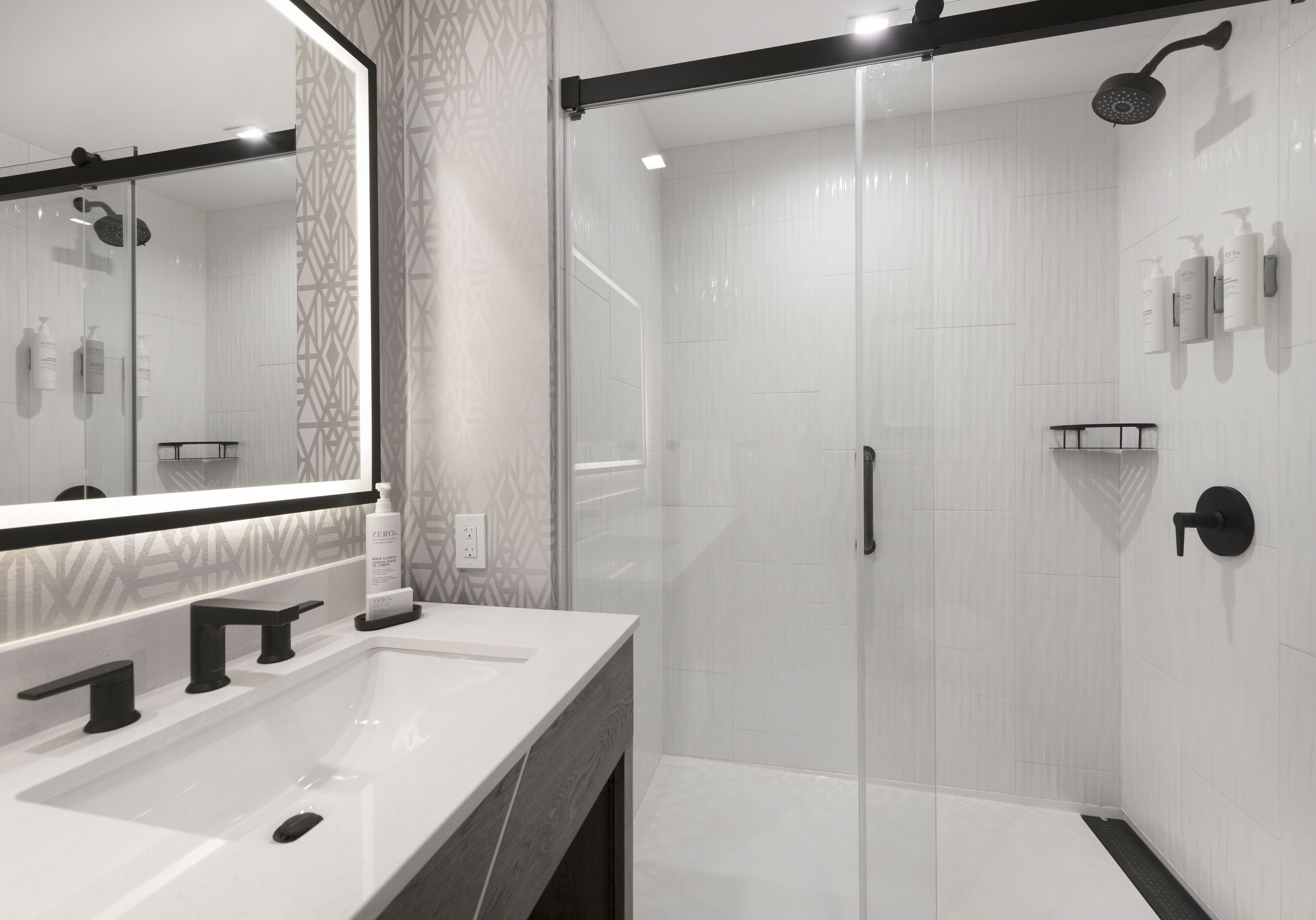 A modern bathroom with a large mirror, a white sink, a glass-enclosed shower, and a black towel rack.