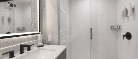 Un baño moderno con un espejo grande, un lavamanos blanco, una ducha con mampara de vidrio y un toallero negro.