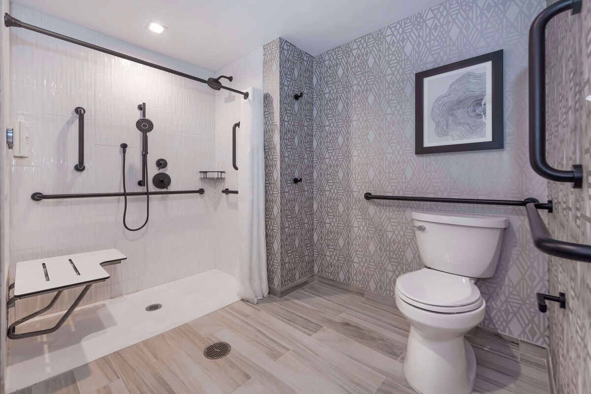 A modern bathroom with a walk-in shower, grab bars, a toilet, and a sink.