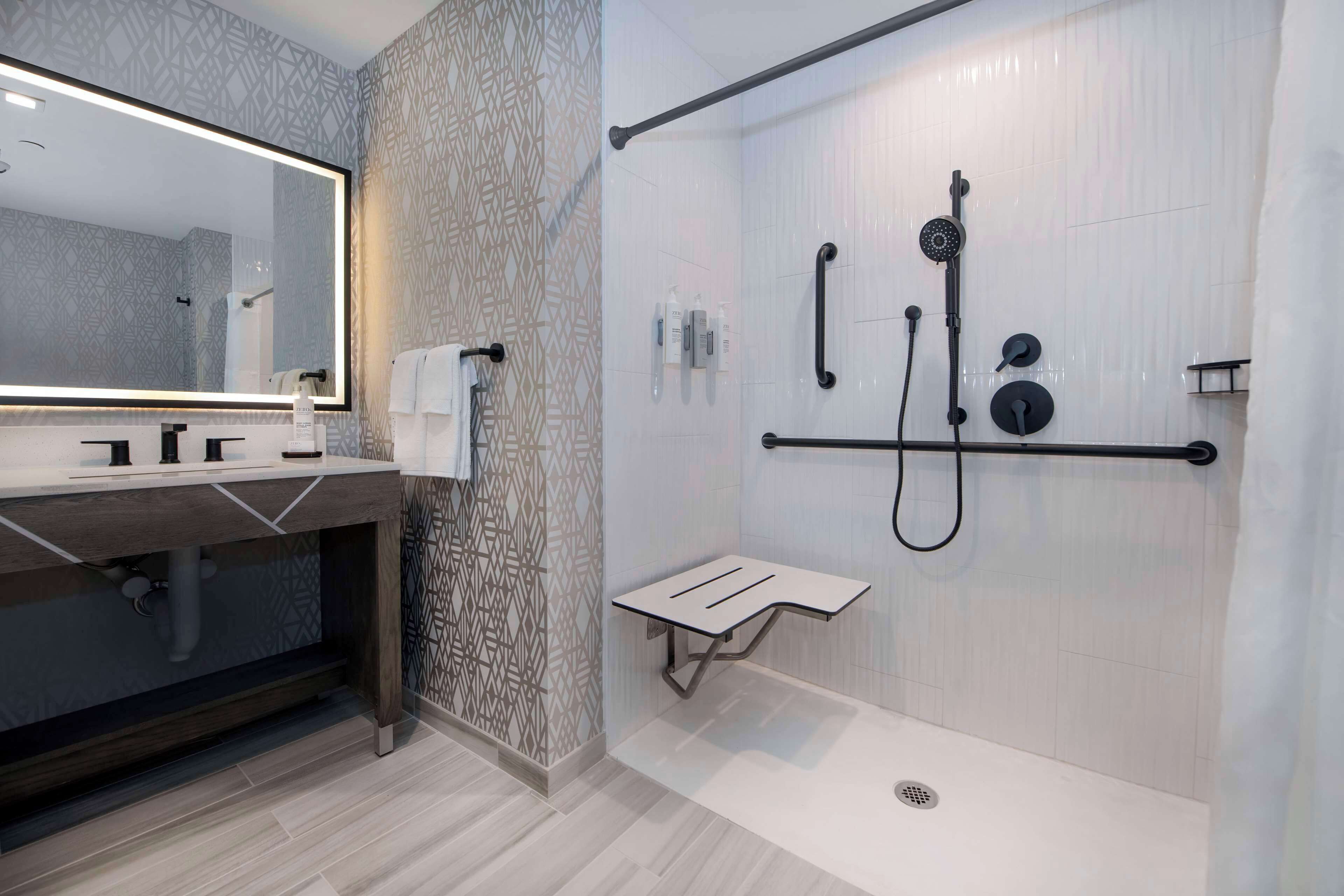 Un baño moderno con un espejo grande, una ducha con cabezal de ducha manual y un perchero para toallas.