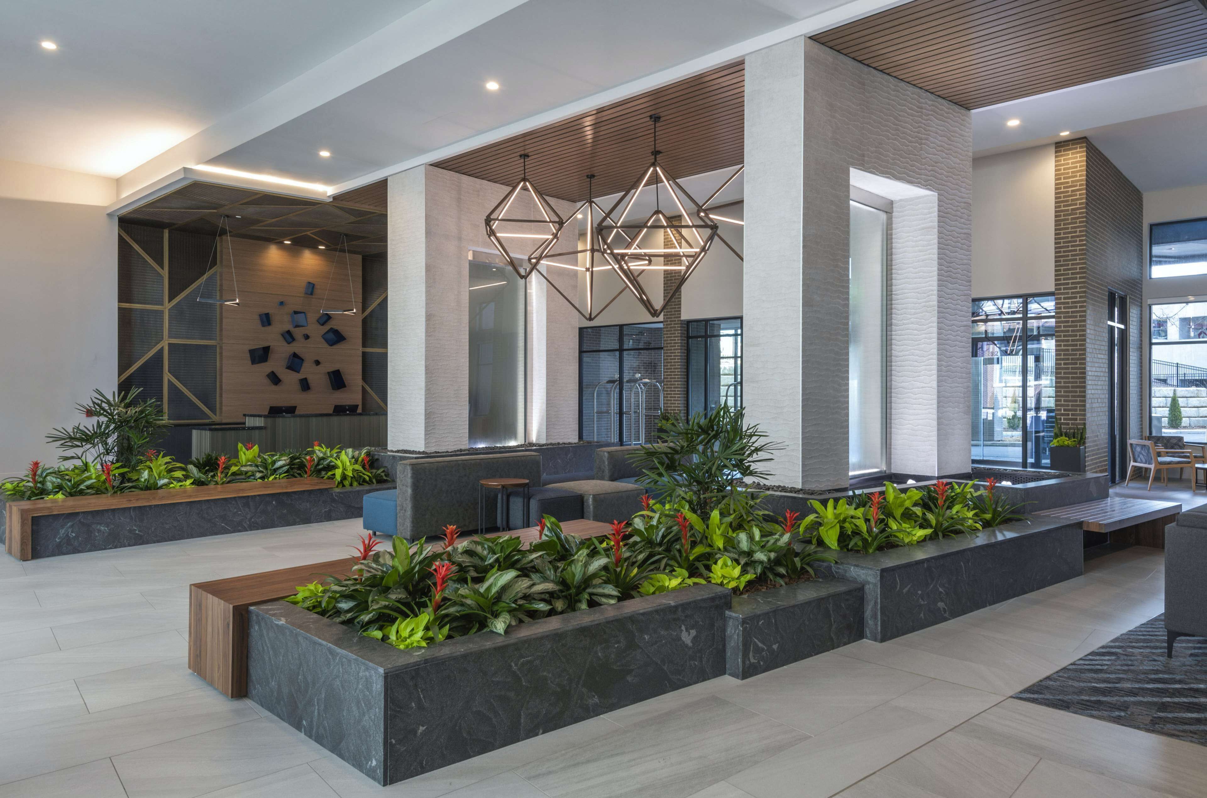 Un vestíbulo moderno con lámparas de diseño geométrico, zonas de estar y plantas de interior.