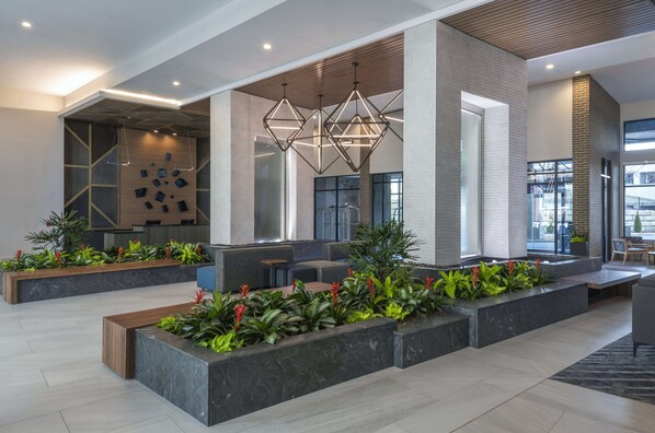Un hall d’entrée moderne agrémenté de luminaires aux formes géométriques, d’espaces de détente et de plantes d’intérieur.