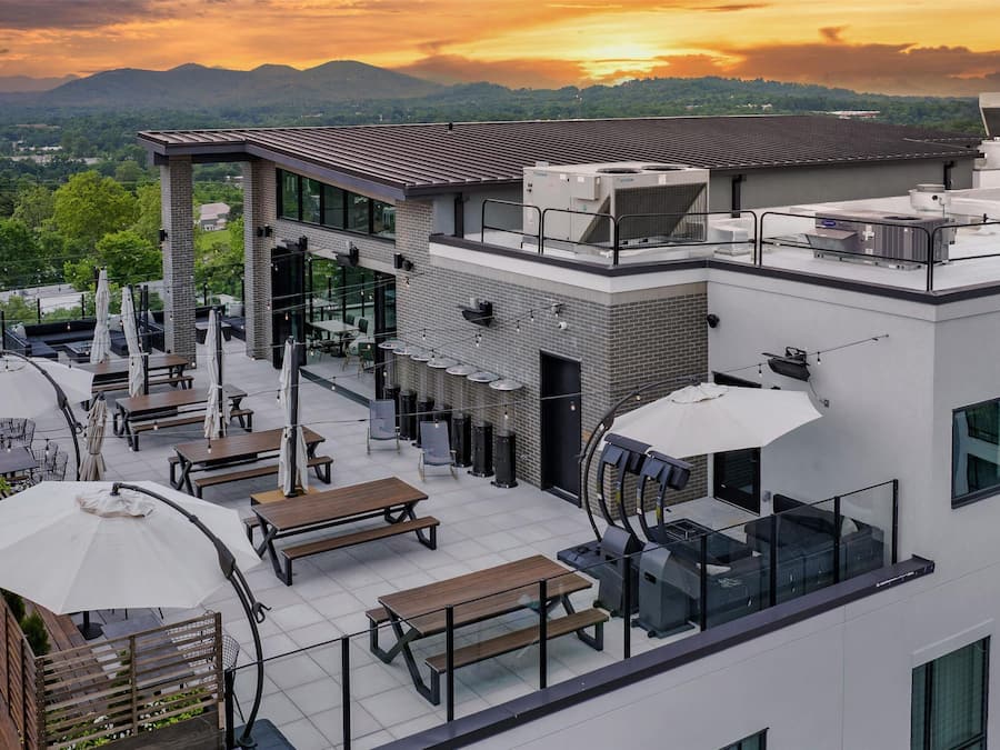 A rooftop terrace with outdoor seating, a glass-enclosed area, and a view of the surrounding landscape.