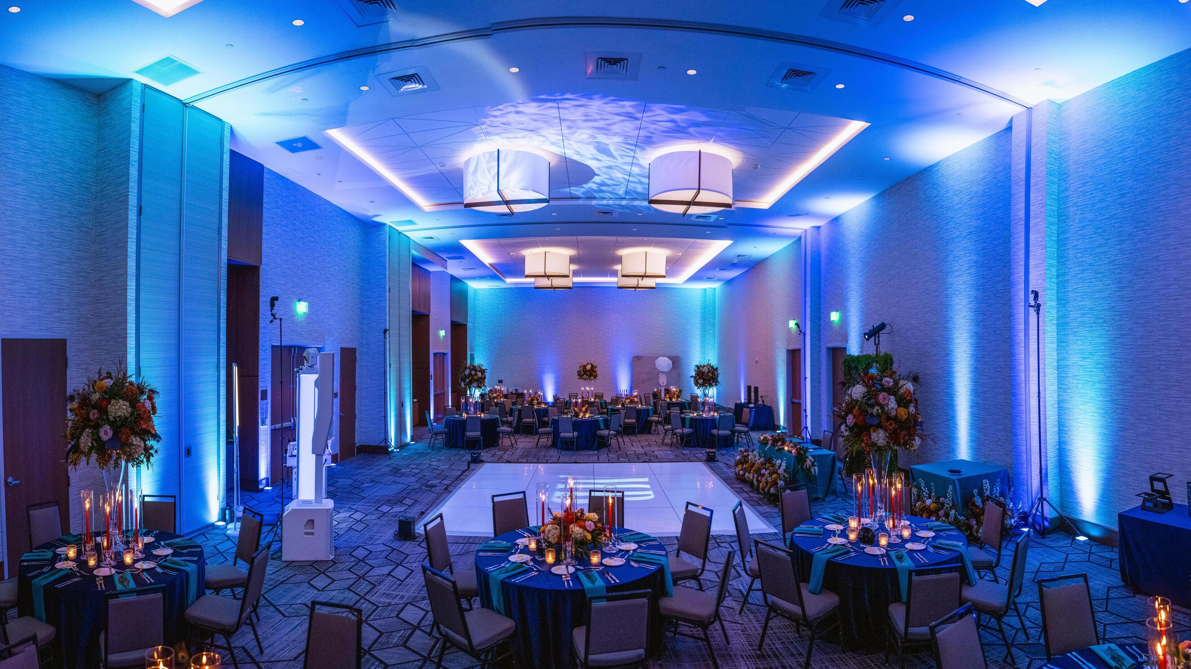 Une salle de banquet spacieuse, avec des tables rondes, des chaises et une scène à l’avant.