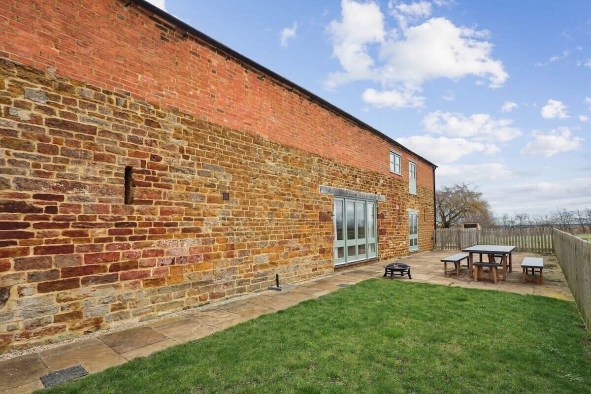 A brick building with a patio area, a wooden fence, and a table with benches.