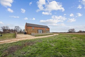 A brick building with a large door and windows, surrounded by a grassy field and a dirt path.