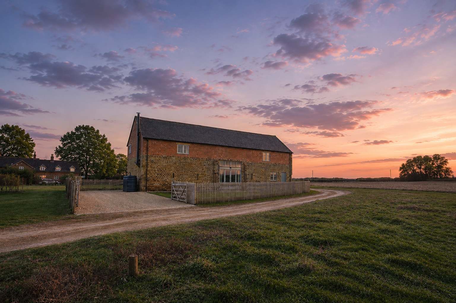 A brick farmhouse with a gravel driveway and a wooden fence.