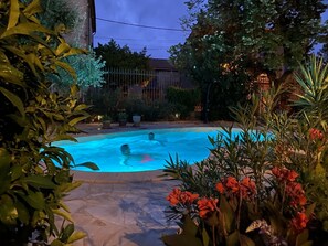 A swimming pool surrounded by potted plants and a stone patio. - Maison de Midi (Ginestas)