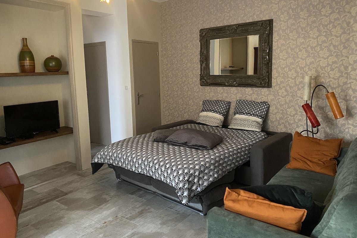A modern bedroom with a bed, a television, a sofa, and a mirror.
