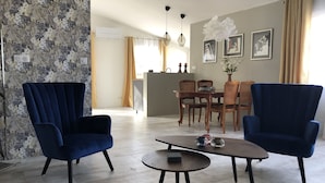 A living room with two blue armchairs, a round coffee table, and a dining area with wooden furniture. - Maison de Midi (Ginestas)
