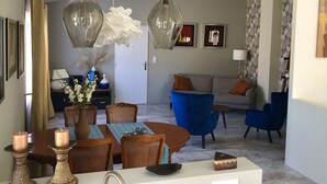 A modern living room with a dining area, featuring a sofa, blue chairs, and a dining table with candles. - Maison de Midi (Ginestas)