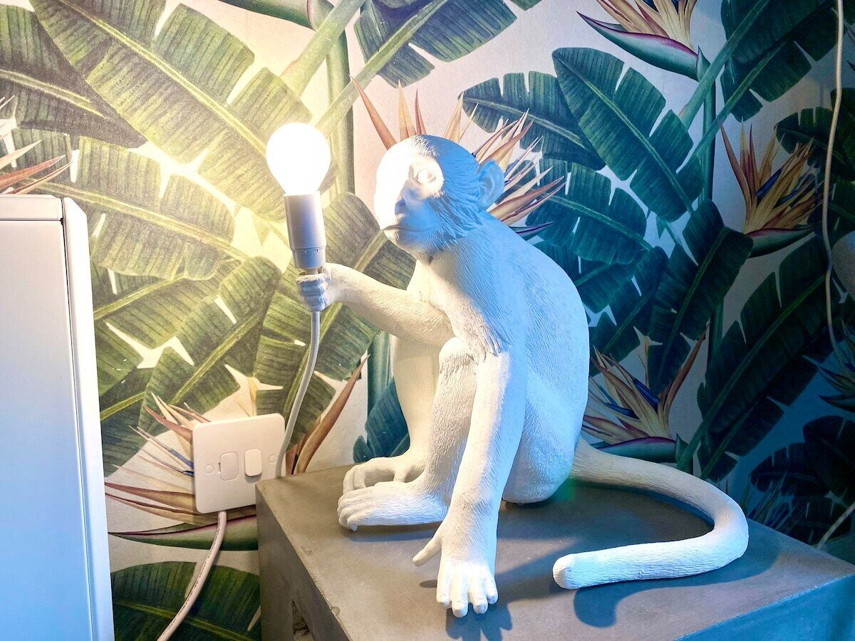 Une sculpture représentant un singe tenant une ampoule, le tout mis en valeur par un décor de grandes feuilles tropicales.