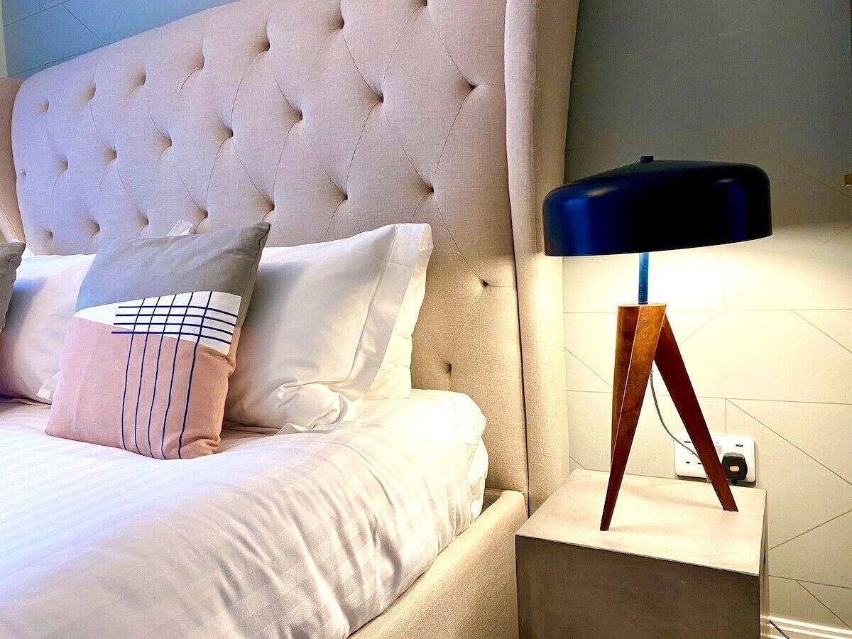 A bed with a tufted headboard, a bedside table with a lamp, and two pillows.