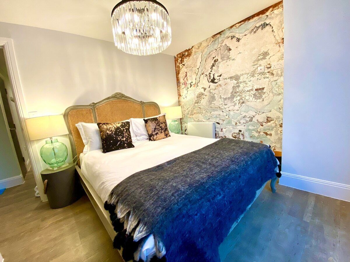 A bedroom with a large bed, a chandelier, a textured wall, and a small side table.
