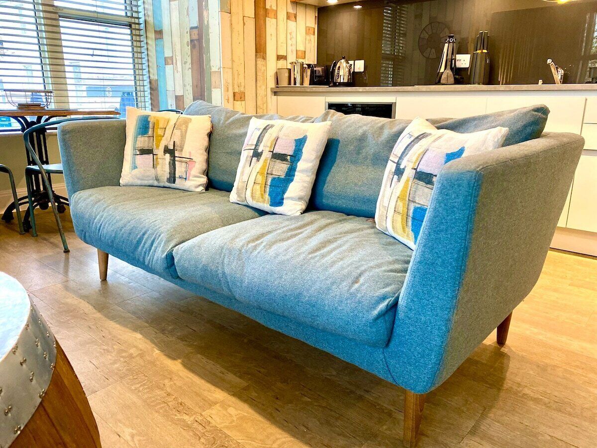 A blue sofa with patterned cushions in a room with wooden flooring and a kitchen area in the background.