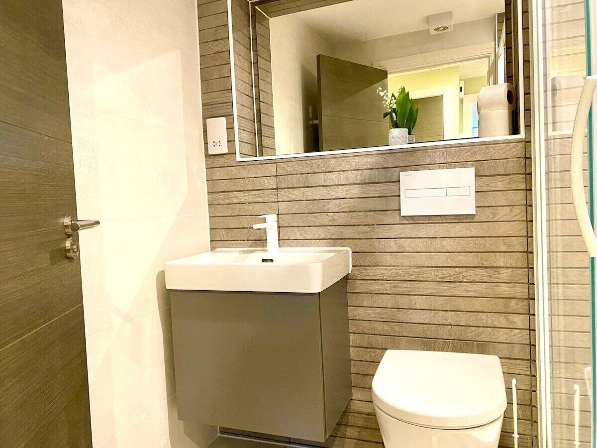 A bathroom with a wooden wall, a white sink, a toilet, and a mirror.