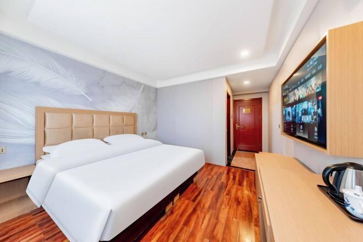 Une chambre d’hôtel avec un lit double, un plancher en bois, un téléviseur fixé au mur et un petit bureau avec une bouilloire.