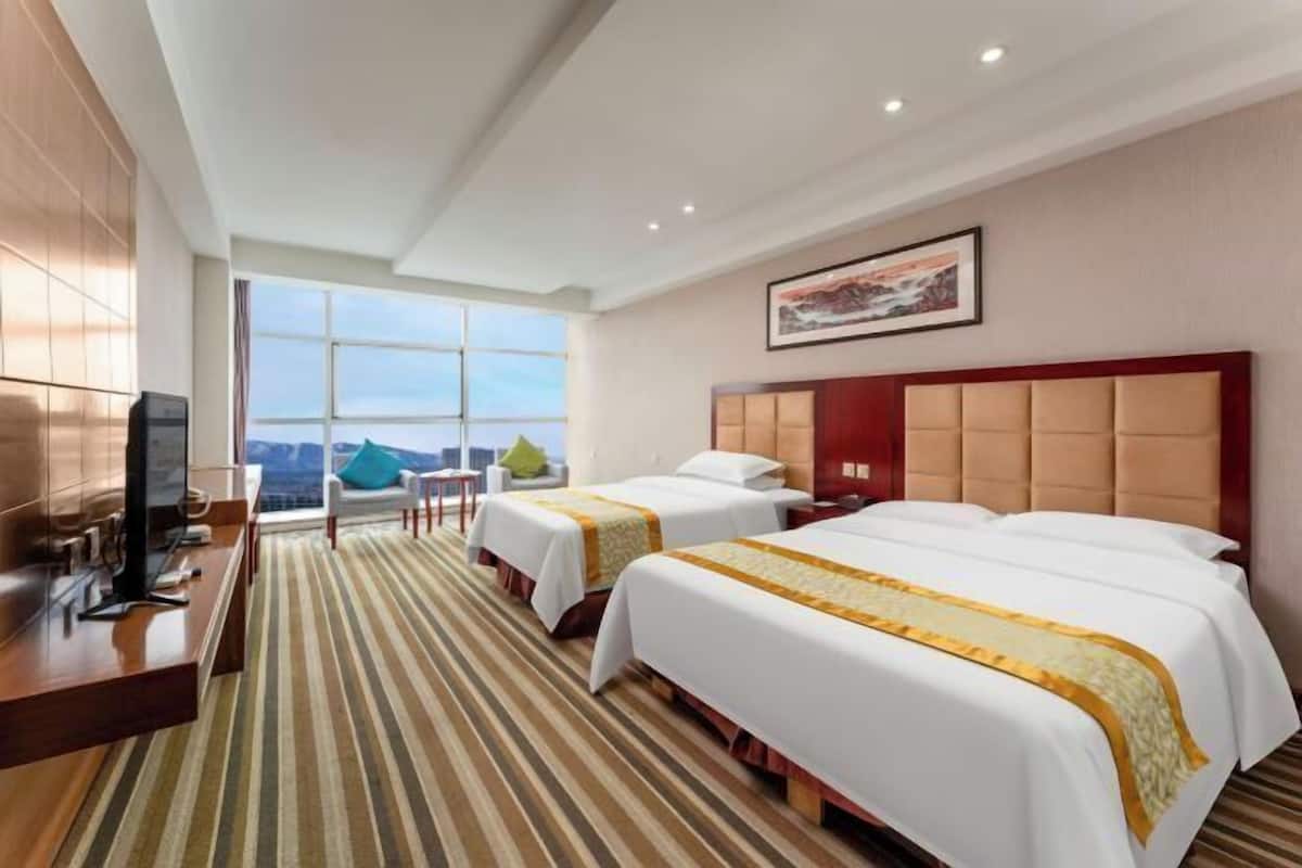Une chambre d’hôtel avec deux lits, une télévision, un bureau et une grande fenêtre donnant sur un beau paysage.