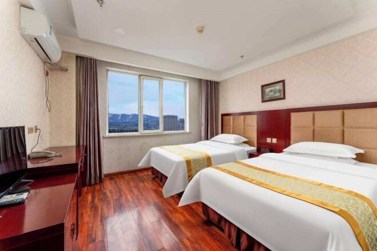 Une chambre d’hôtel avec deux lits, un bureau, un appareil de climatisation, une fenêtre avec vue et un tableau encadré au mur.