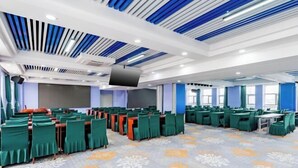 Une grande salle de conférence avec des rangées de tables et de chaises, un téléviseur à écran plat et une moquette à motifs.