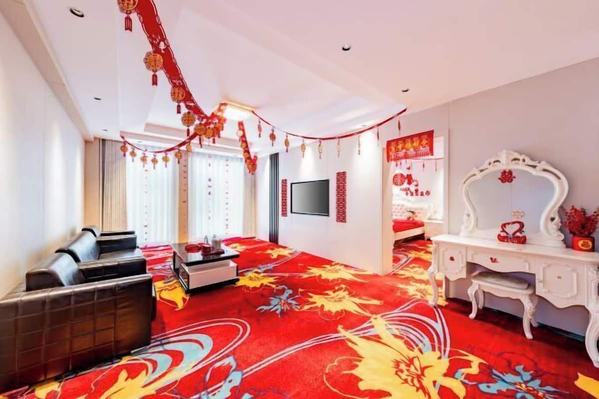Une chambre d’hôtel avec un tapis rouge, un canapé, une télévision, un bureau et un miroir.