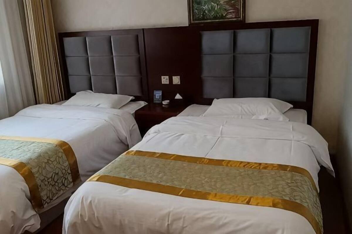 Une chambre d’hôtel avec deux lits, une tête de lit sombre et une petite table de chevet avec une lampe.