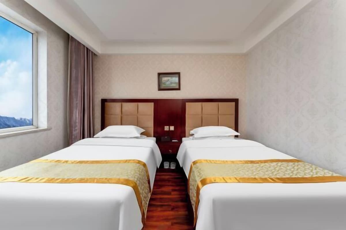 A hotel room with two beds, a wooden headboard, a small window, and a door.